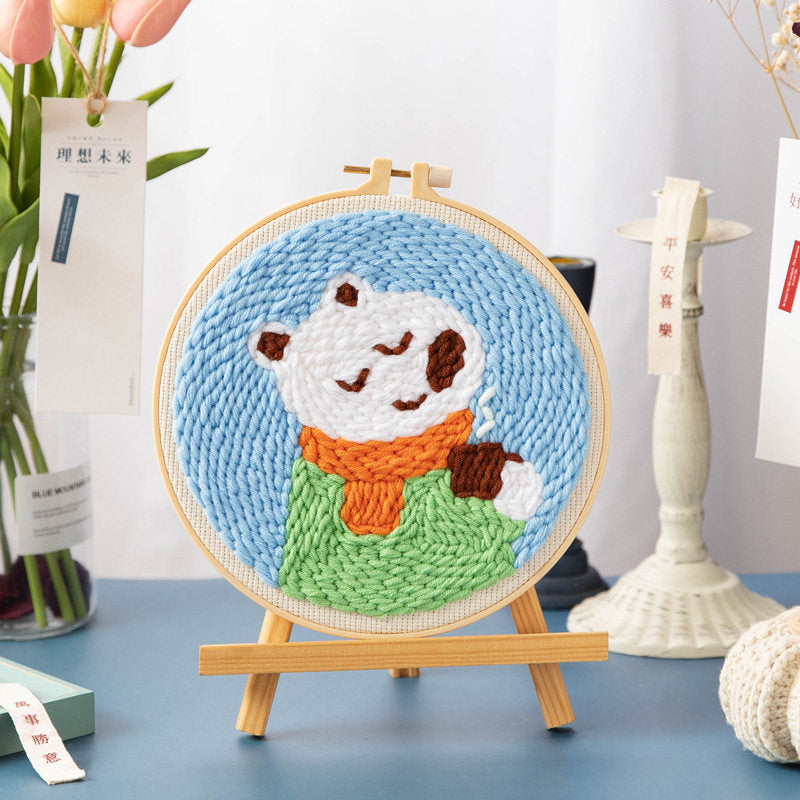 Bundled Bear Cub Punch Needle Kit - white polar bear wearing an orange scarf and green sweater design on a light blue background