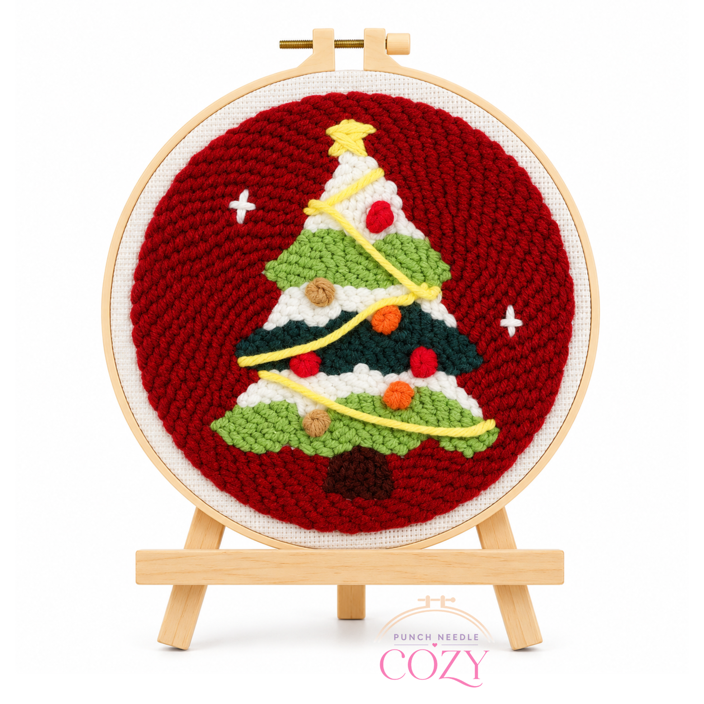 Cross-stitched Christmas tree design on a red background with a wooden hoop and easel.