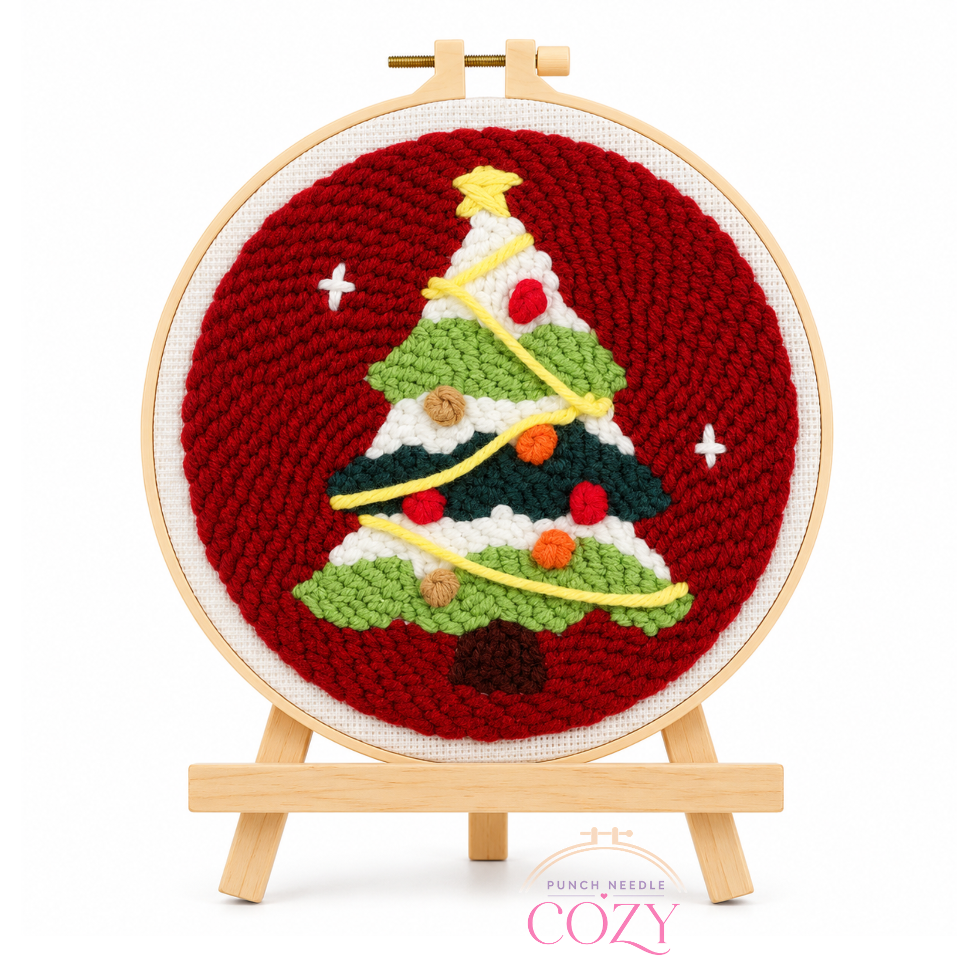 Cross-stitched Christmas tree design on a red background with a wooden hoop and easel.