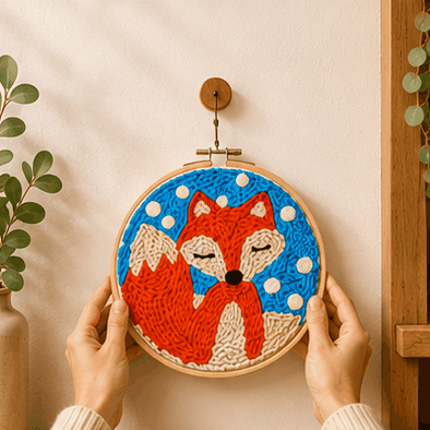 Punch needle embroidery hoop with a fox design on a blue background, hung on a wall.
